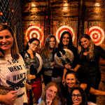 Group of women smiling and holding axes at an indoor axe throwing venue in Hollywood Florida