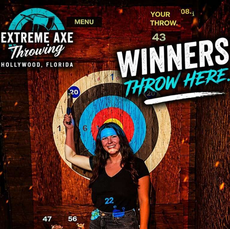 Woman holding axe and smiling after a successful throw at Extreme Axe Throwing Hollywood Florida