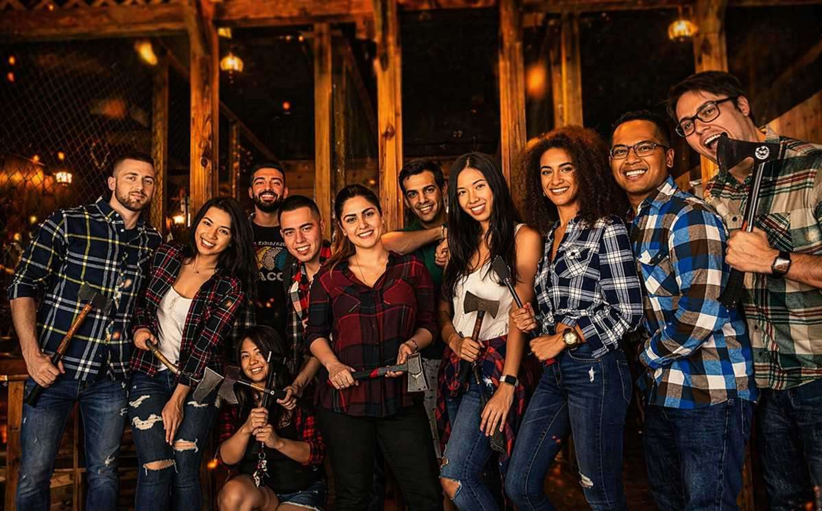 Large group of friends smiling and holding axes at an indoor axe throwing venue in Hollywood Florida