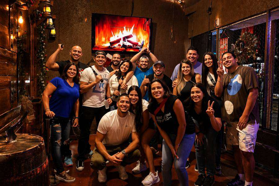 Group of friends celebrating together inside Extreme Axe Throwing in Hollywood Florida, smiling and posing in a warm rustic venue atmosphere